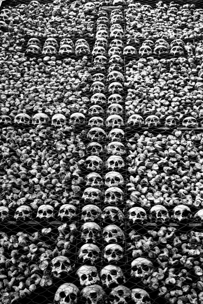 black and white photo, with skulls, some of the skulls form a cross, they are behind a fence.